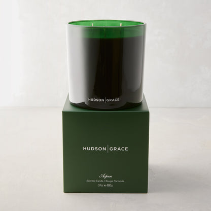 Hudson Grace Aspen 3-wick candle in a dark green glass vessel, atop a matching green gift box.