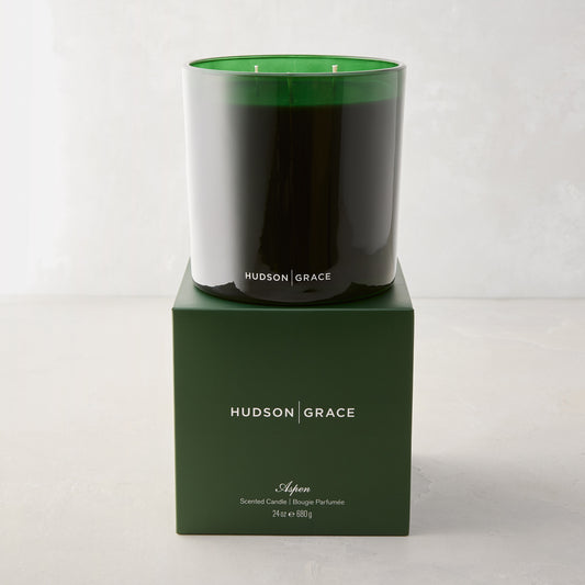 Hudson Grace Aspen 3-wick candle in a dark green glass vessel, atop a matching green gift box.
