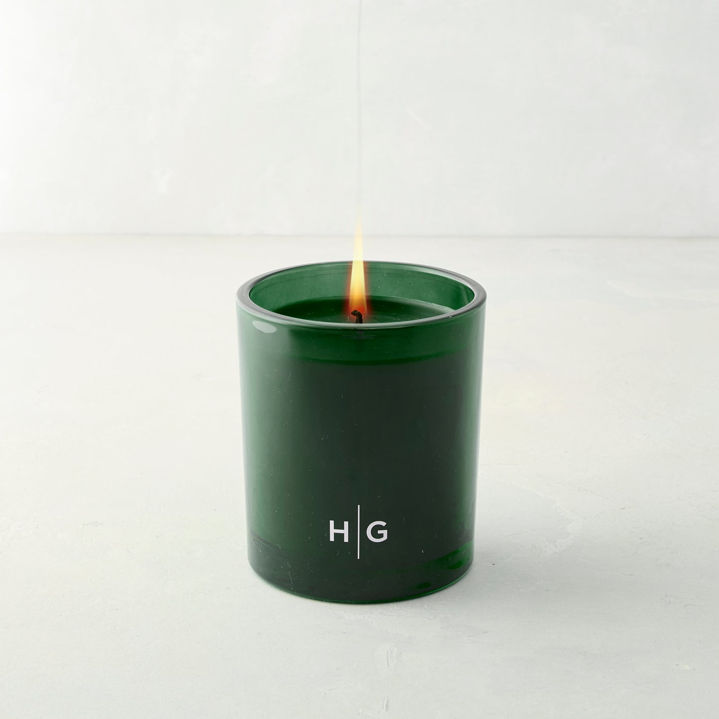 Hudson Grace Aspen Fir scented candle in a dark green glass vessel with "HG" logo, lit wick.
