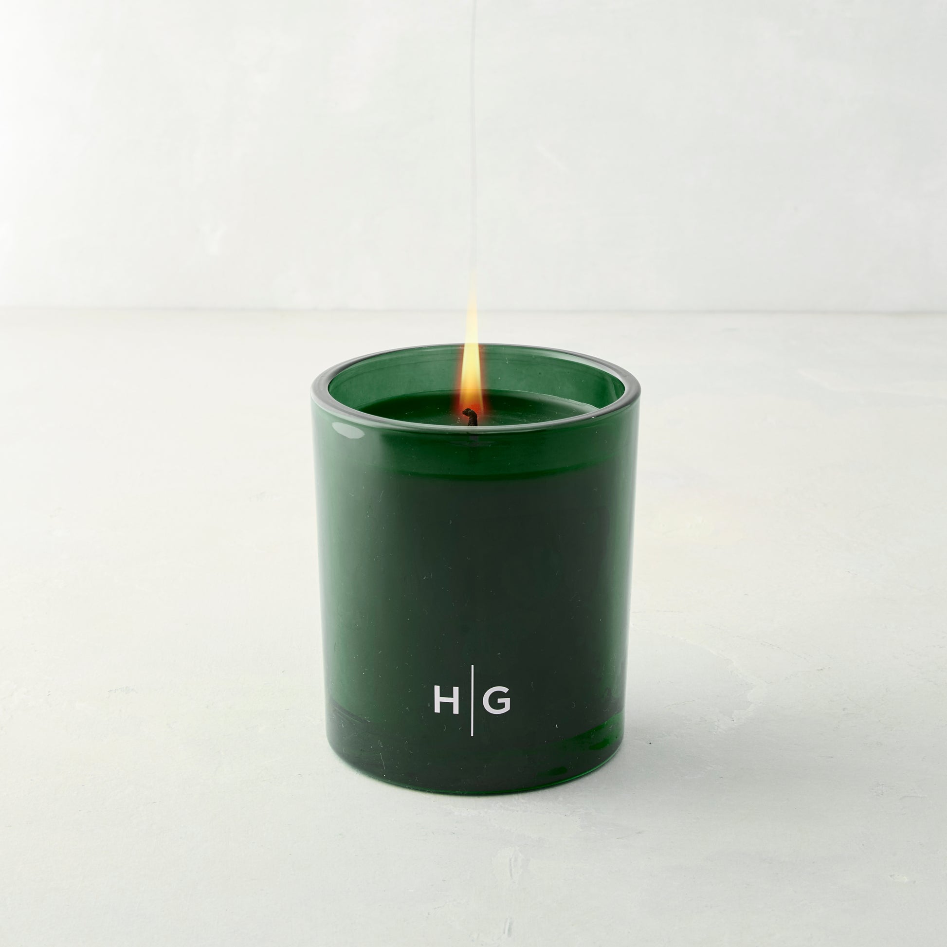 Hudson Grace Aspen Fir scented candle in a dark green glass vessel with "HG" logo, lit wick.