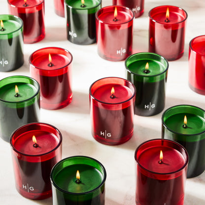 Hudson Grace Aspen Fir scented candles in red and green glass vessels with lit wicks.
