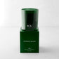 Hudson Grace Aspen Scented Candle in a dark green glass vessel with "HG" logo, atop its matching green box.