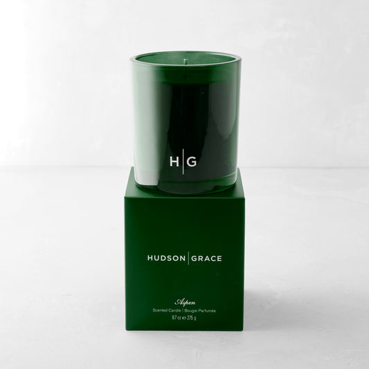 Hudson Grace Aspen Scented Candle in a dark green glass vessel with "HG" logo, atop its matching green box.