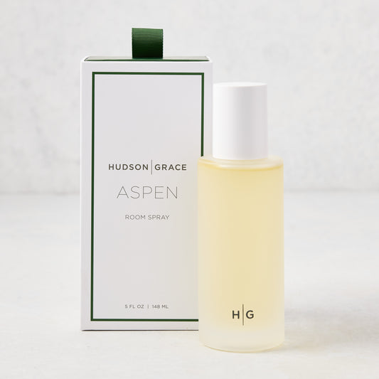 Aspen room spray in a frosted glass bottle with a white cap, standing next to its white and green branded box.