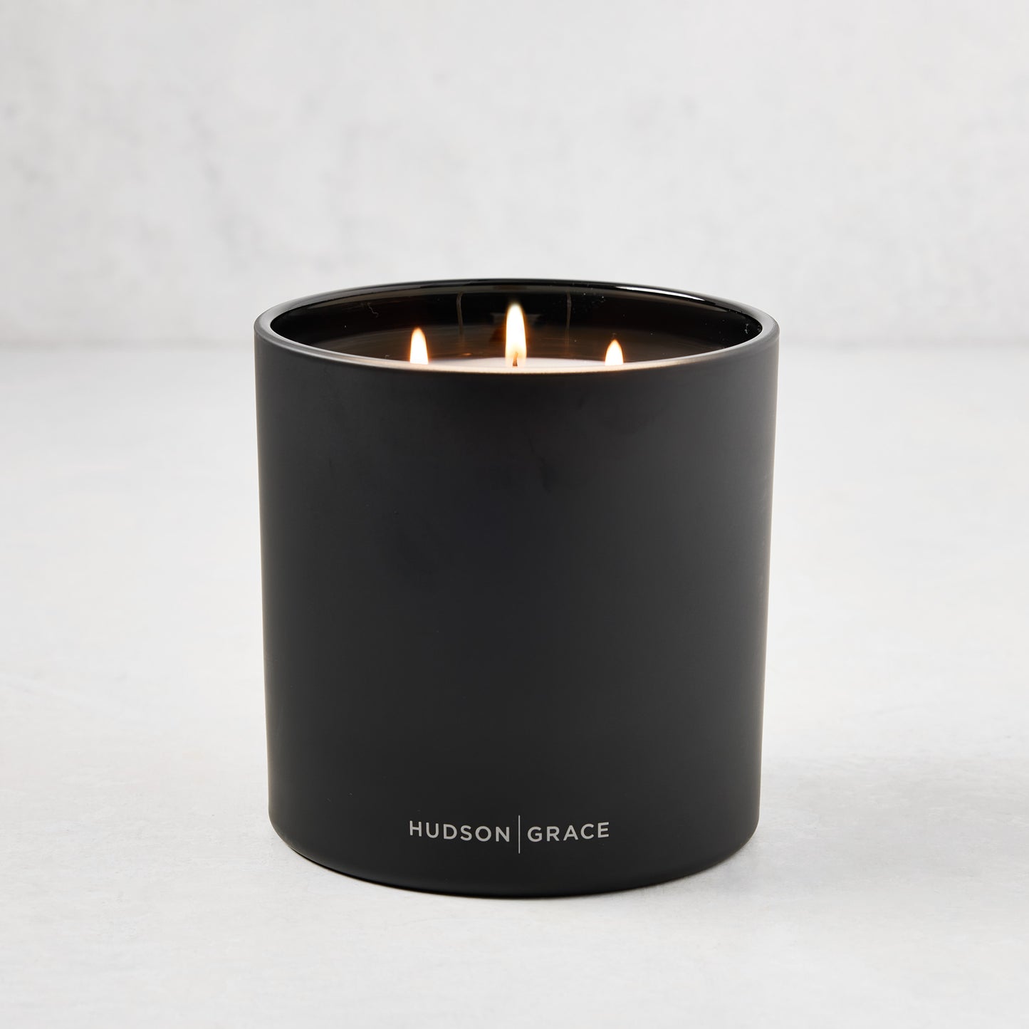 Hudson Grace Bleecker Scented 3-Wick Candle in a matte black heavyweight glass vessel, lit.