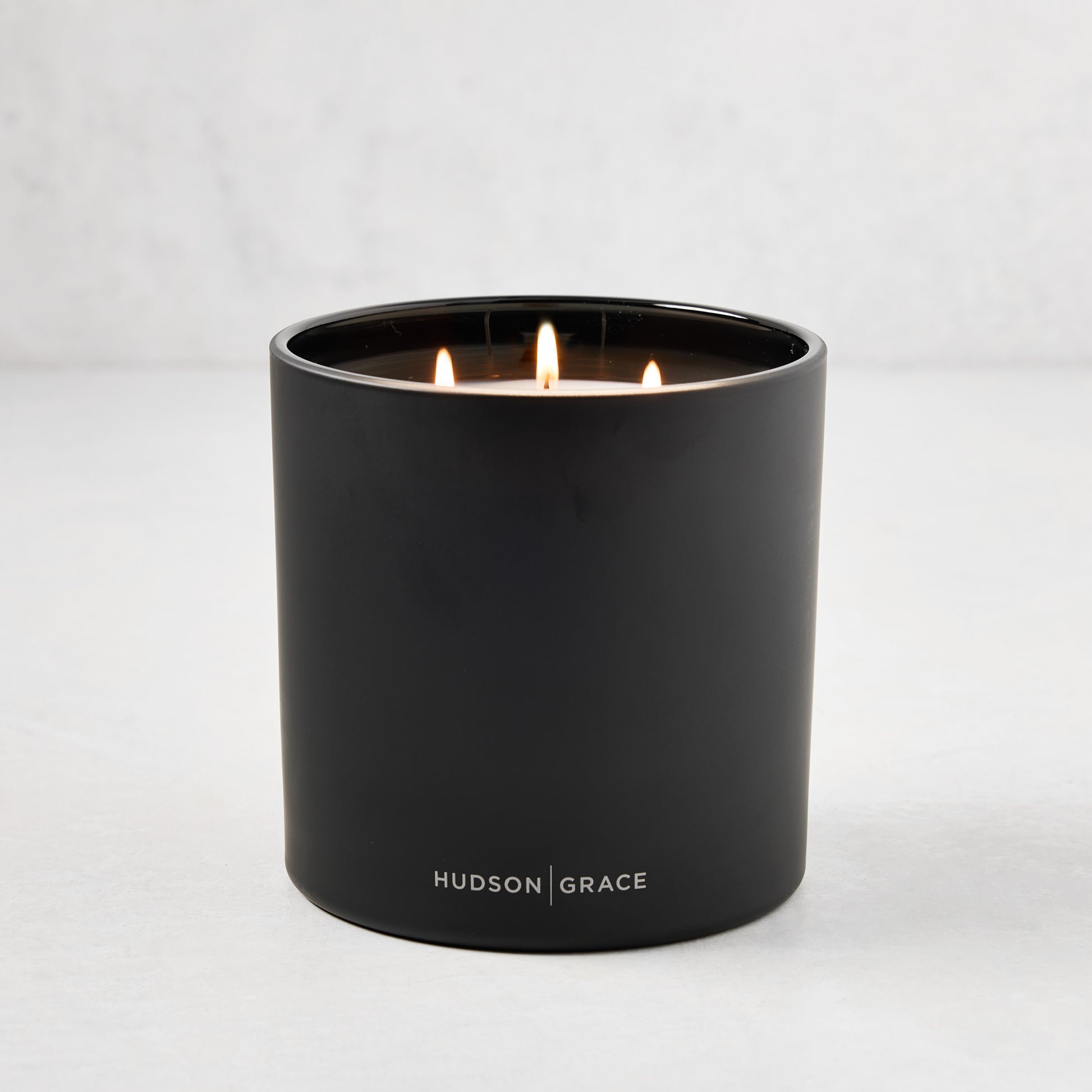 Hudson Grace Bleecker Scented 3-Wick Candle in a matte black heavyweight glass vessel, lit.
