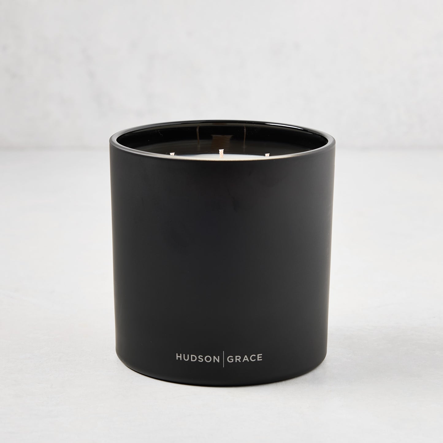 Hudson Grace Bleecker 3-wick candle in a matte black heavyweight glass vessel with white text logo.