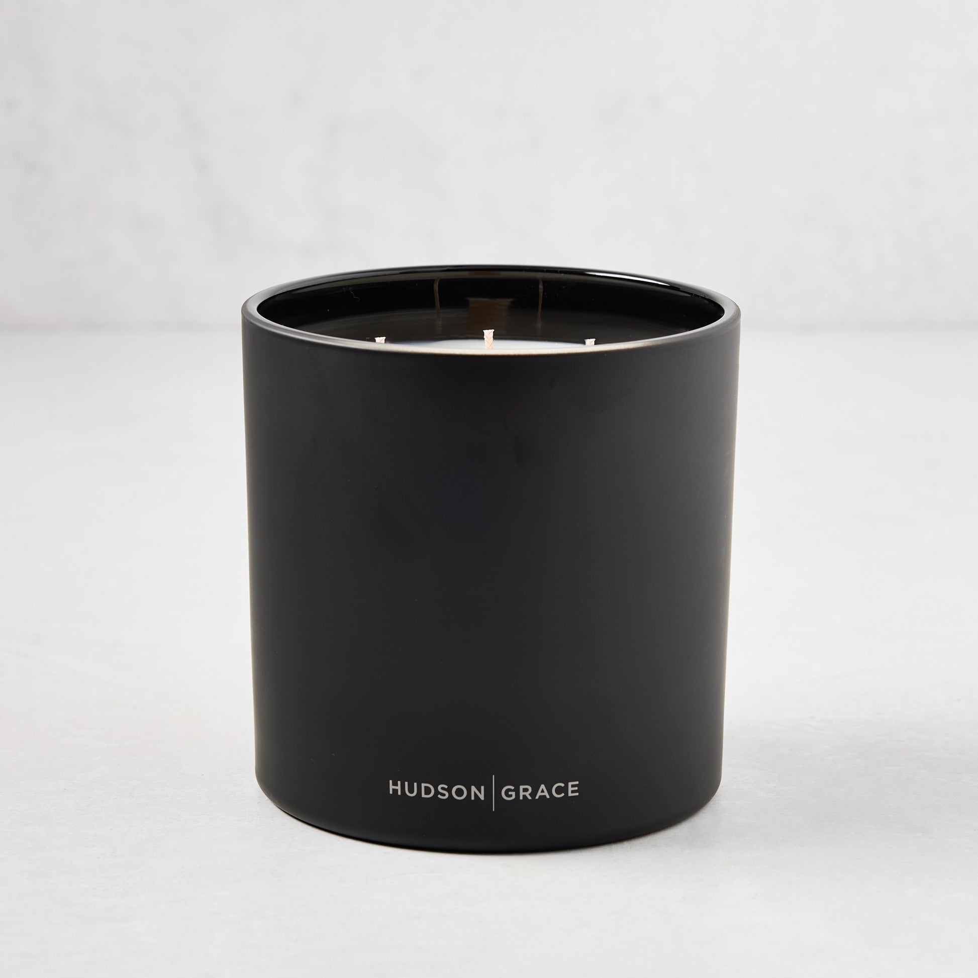 Hudson Grace Bleecker 3-wick candle in a matte black heavyweight glass vessel with white text logo.