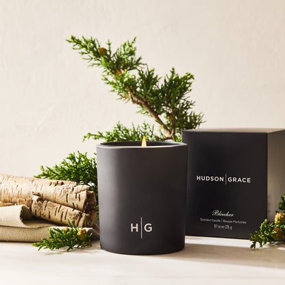 Hudson Grace Bleecker scented candle in a matte black glass vessel with a lit wick, next to its black box.