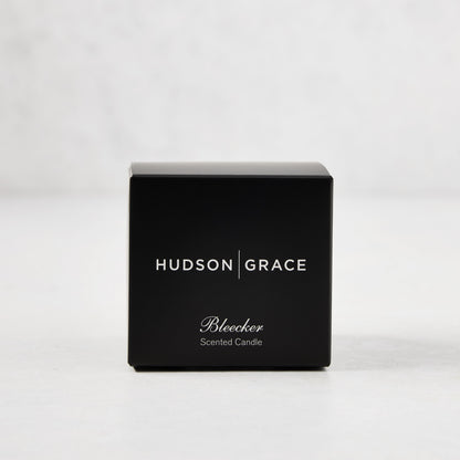 Hudson Grace Bleecker Scented Votive in a black box with white text, on a light background.
