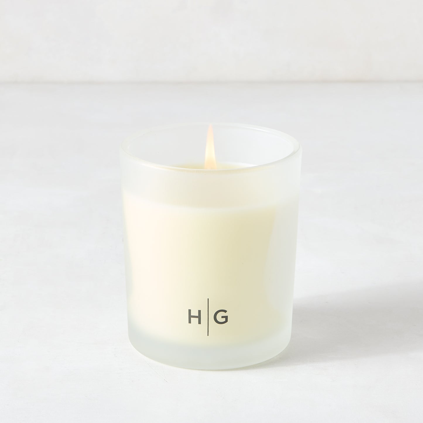 Hudson Grace Brentwood scented candle in a frosted glass vessel with "HG" logo, lit wick.