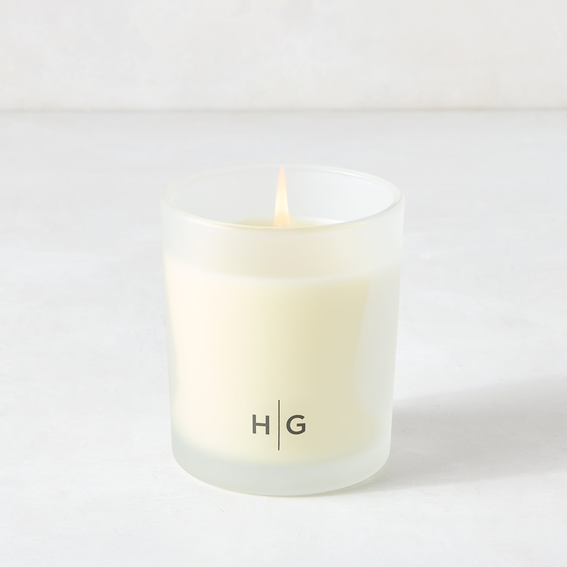 Hudson Grace Brentwood scented candle in a frosted glass vessel with "HG" logo, lit wick.