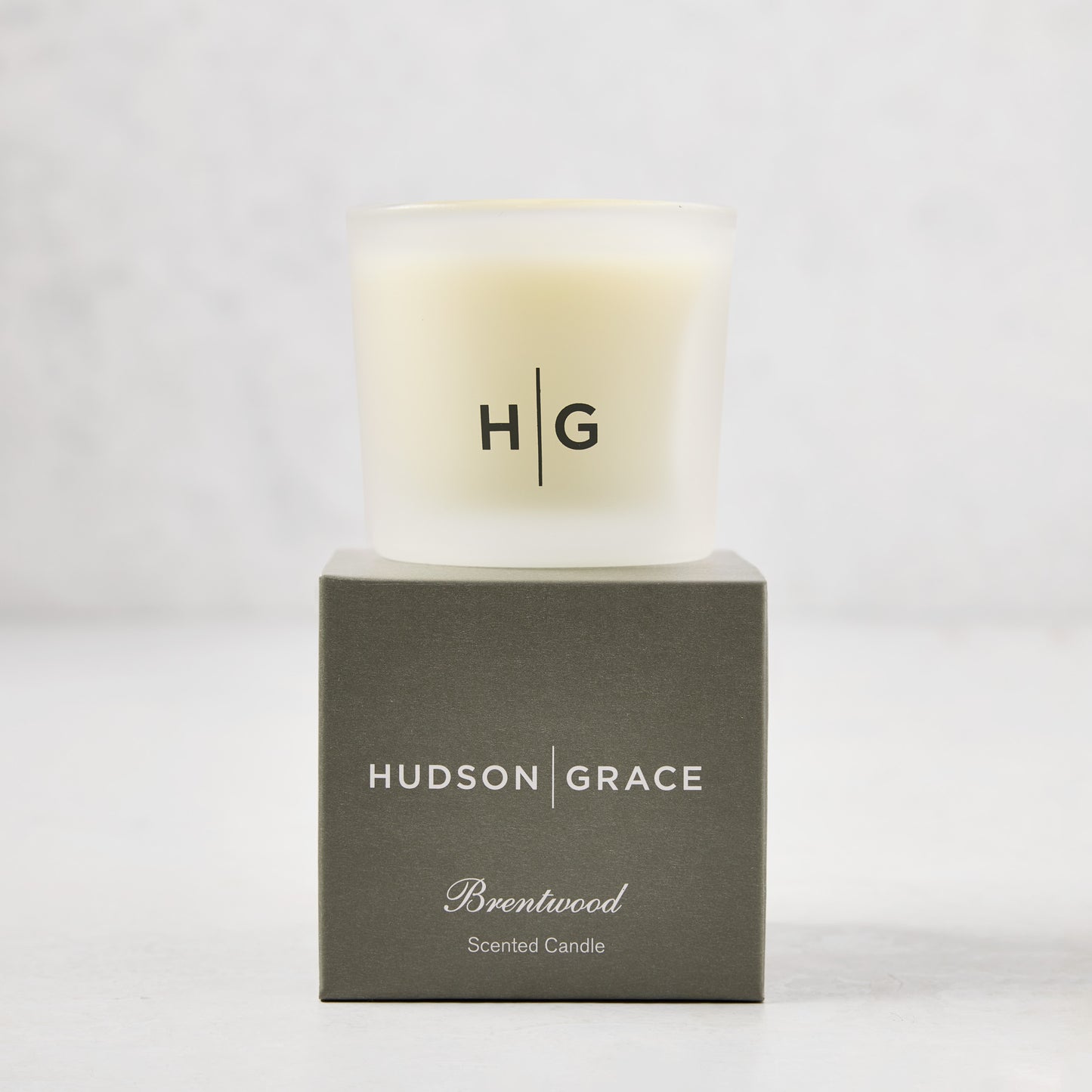 Hudson Grace Brentwood Votive Scented Candle in a frosted glass vessel on its gray gift box.