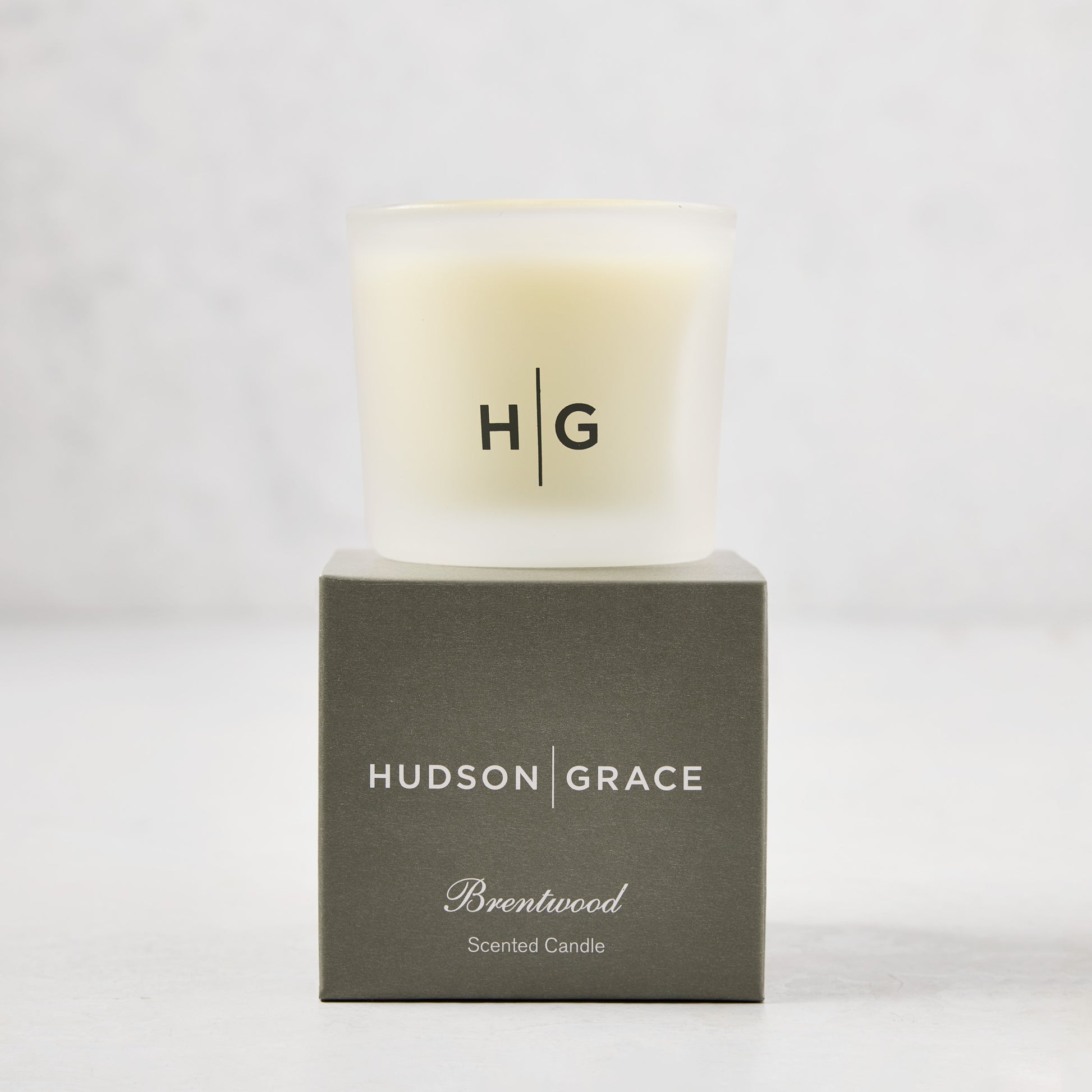 Hudson Grace Brentwood Votive Scented Candle in a frosted glass vessel on its gray gift box.