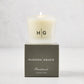 Hudson Grace Brentwood Votive Scented Candle in a frosted glass vessel, lit, on a dark gray box.