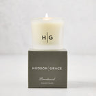 Hudson Grace Brentwood Votive Scented Candle in a frosted glass vessel, lit, on a dark gray box.