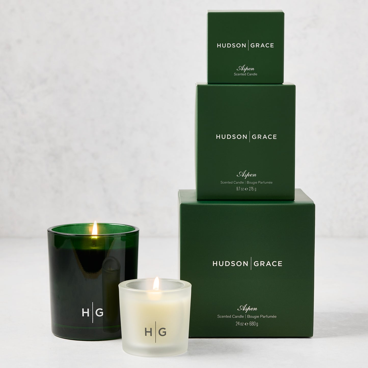 Hudson Grace Aspen Candle Gift Set: three green boxes stacked, two lit candles in green and frosted glass.