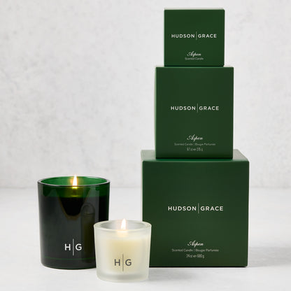 Hudson Grace Aspen Candle Gift Set: three green boxes stacked, two lit candles in green and frosted glass.