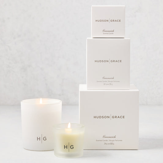 Hudson Grace Greenwich Candle Gift Set: 3 white boxes stacked, 2 lit candles (votive, classic) with HG logo.