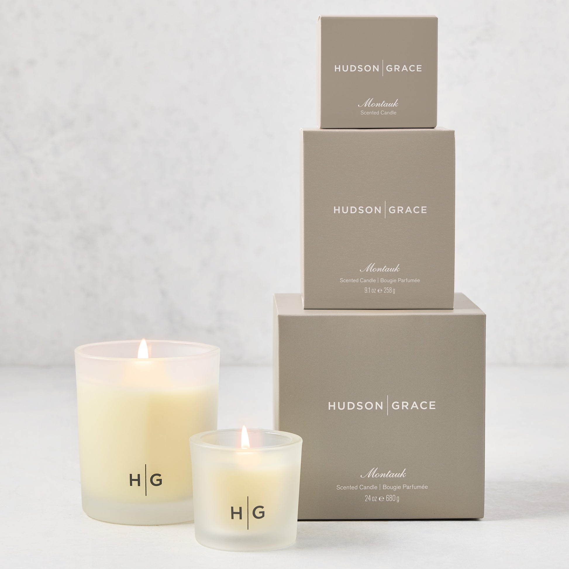 Hudson Grace Montauk Candle Gift Set: 3 frosted glass candles with HG logo and 3 stacked gray boxes.