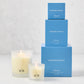 Hudson Grace Montecito Candle Gift Set: 3 blue boxes stacked, 2 lit frosted glass candles with "HG" logo.