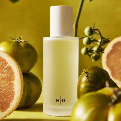 Hudson Grace San Marzano fragrance bottle with green tomatoes and grapefruit slices on a yellow background.