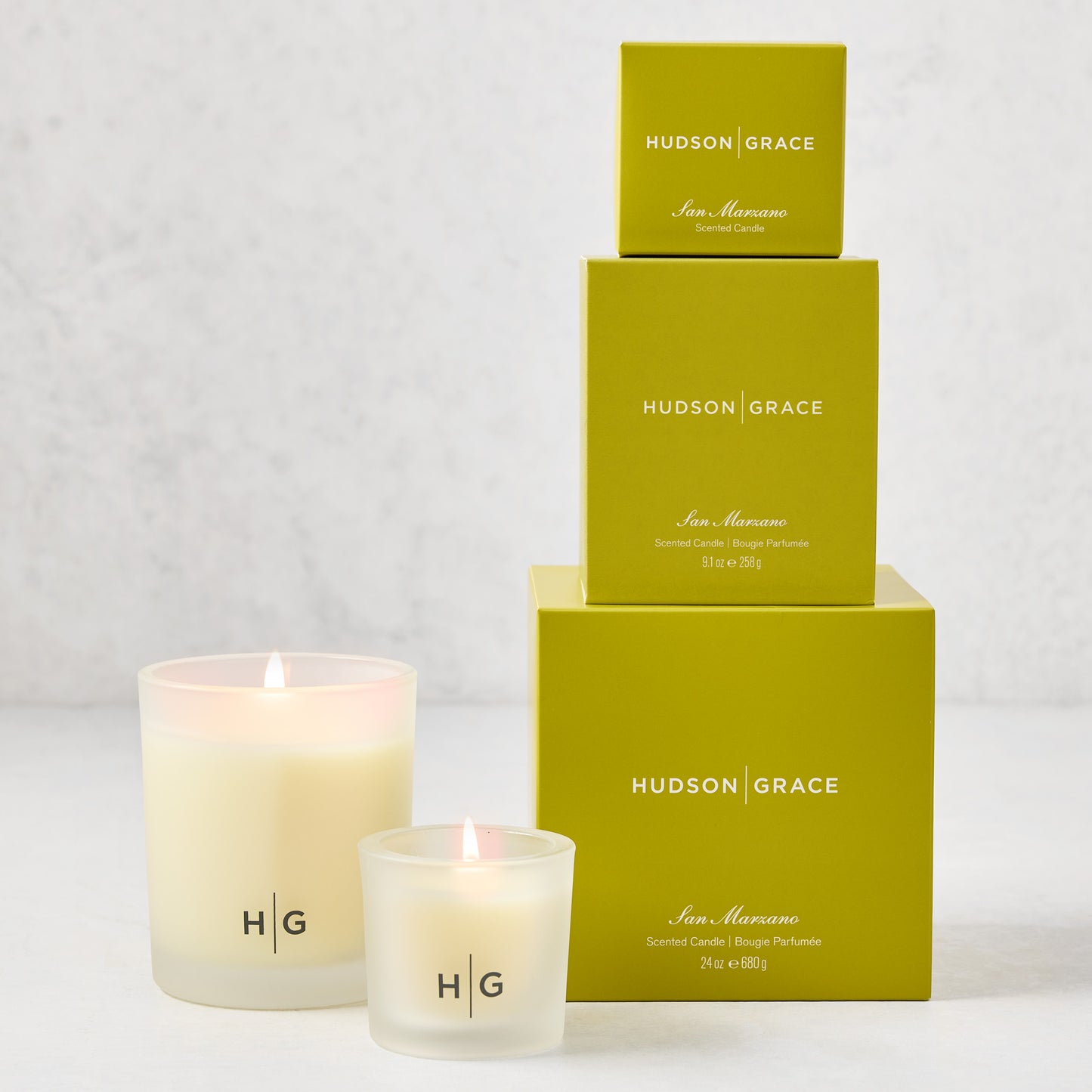 Hudson Grace San Marzano candle gift set: two lit candles in frosted glass, three stacked lime green boxes.