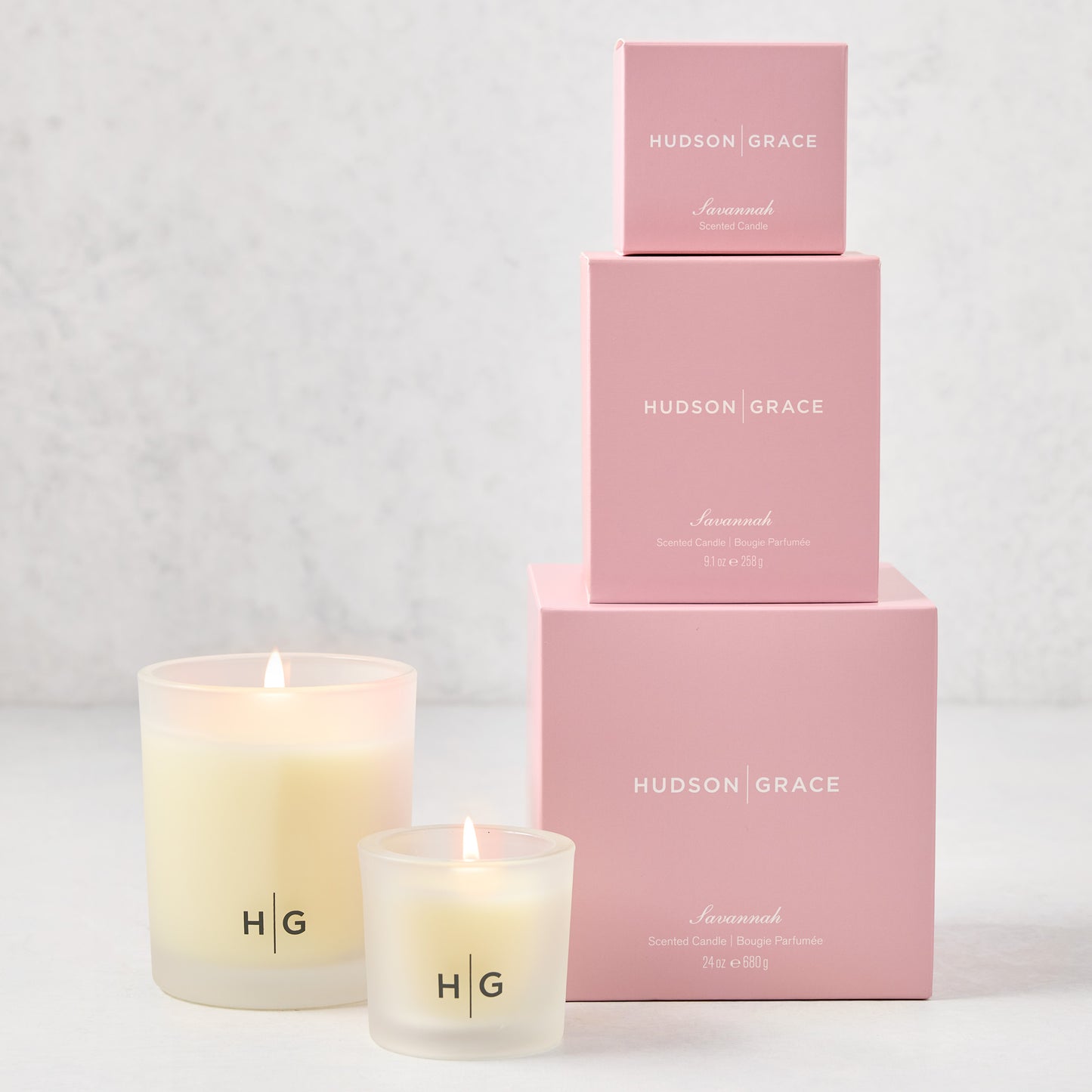 Hudson Grace Savannah candle gift set with two lit frosted glass candles and three pink branded boxes.