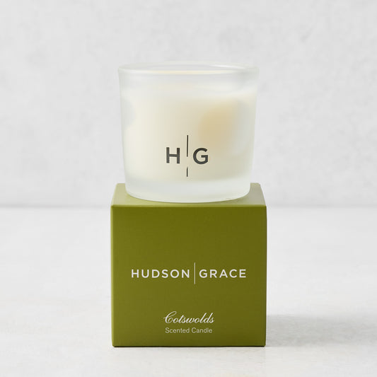 Hudson Grace Cotswolds scented votive candle in a frosted glass vessel resting on a green branded gift box.