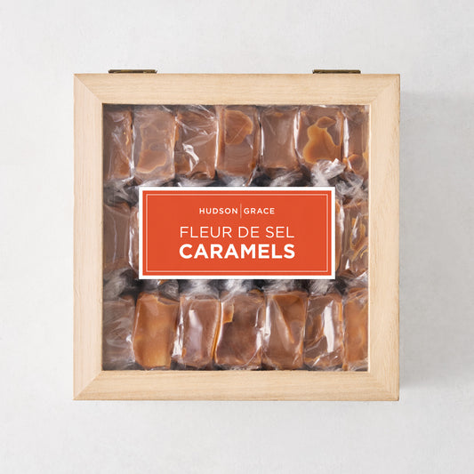 63 Hudson Grace fleur de sel caramels individually wrapped in a square light wood box with a clear lid.