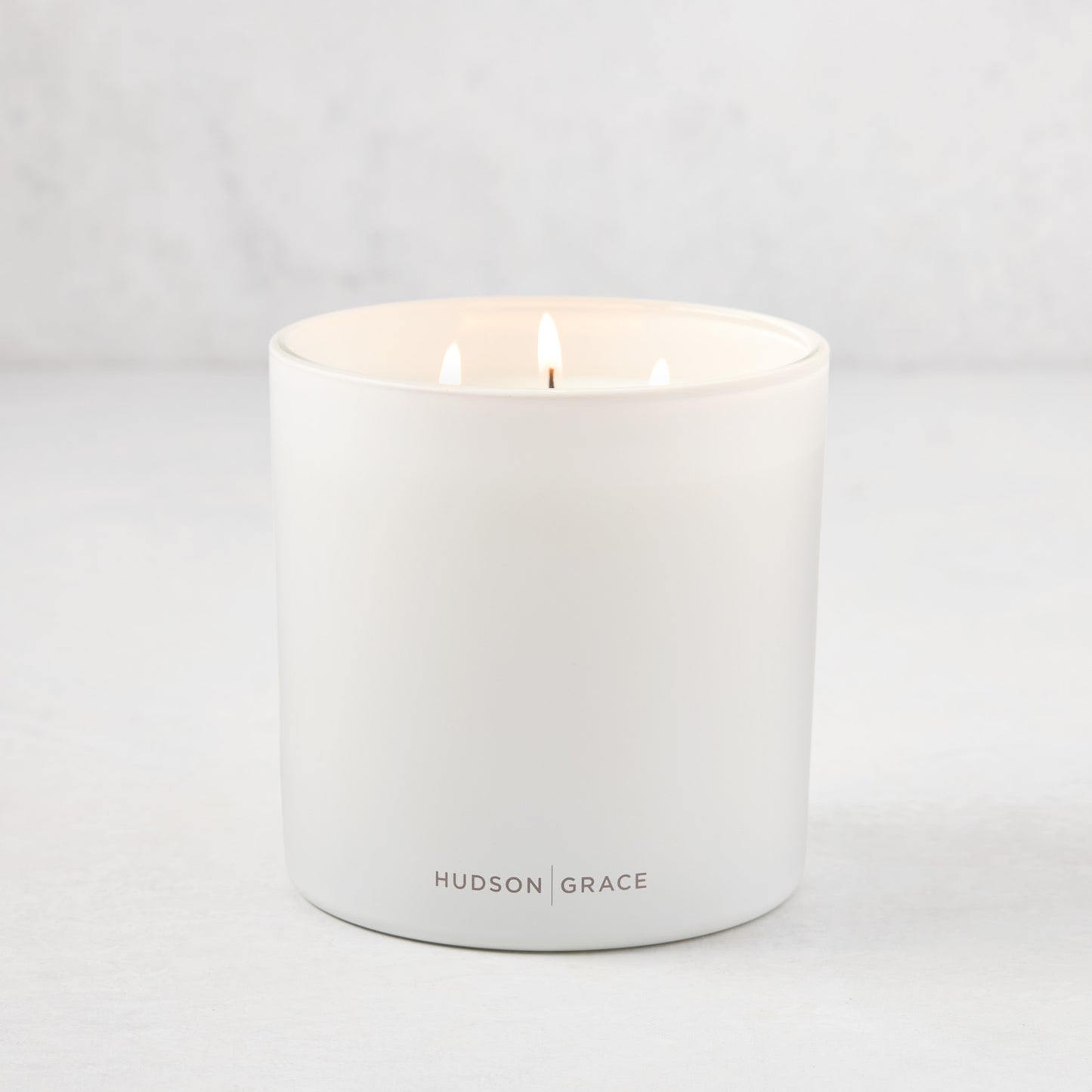 Hudson Grace Greenwich 3-wick candle in a white matte glass vessel with "HUDSON GRACE" logo.