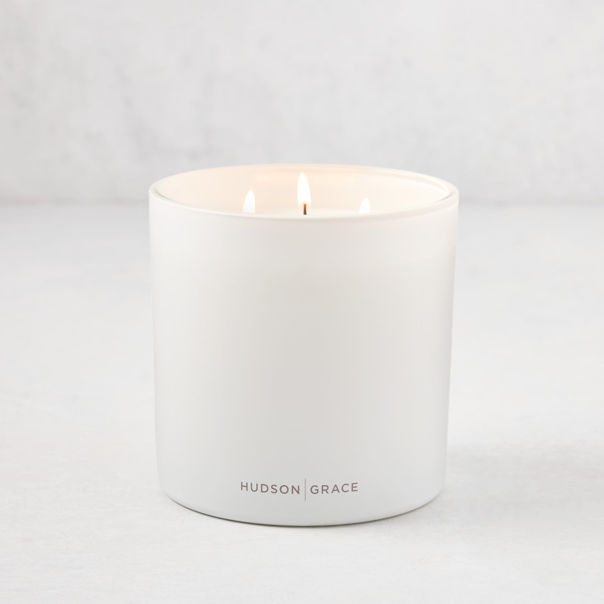 Hudson Grace Greenwich 3-wick candle in a white matte glass vessel with "HUDSON GRACE" logo.