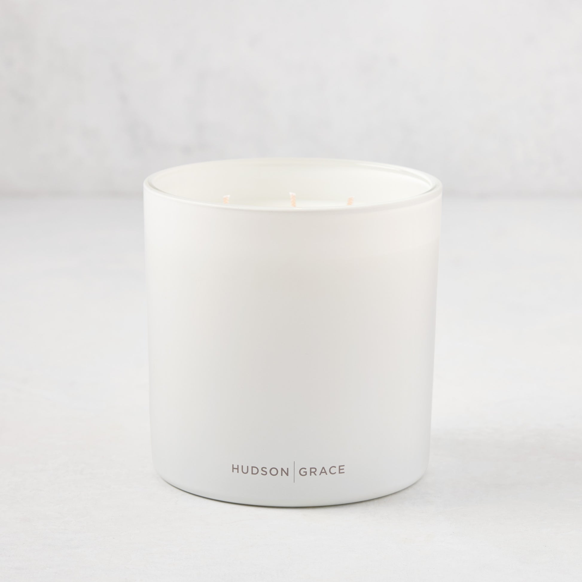 Hudson Grace Greenwich 3-wick candle in a white matte glass vessel with light pink wicks.