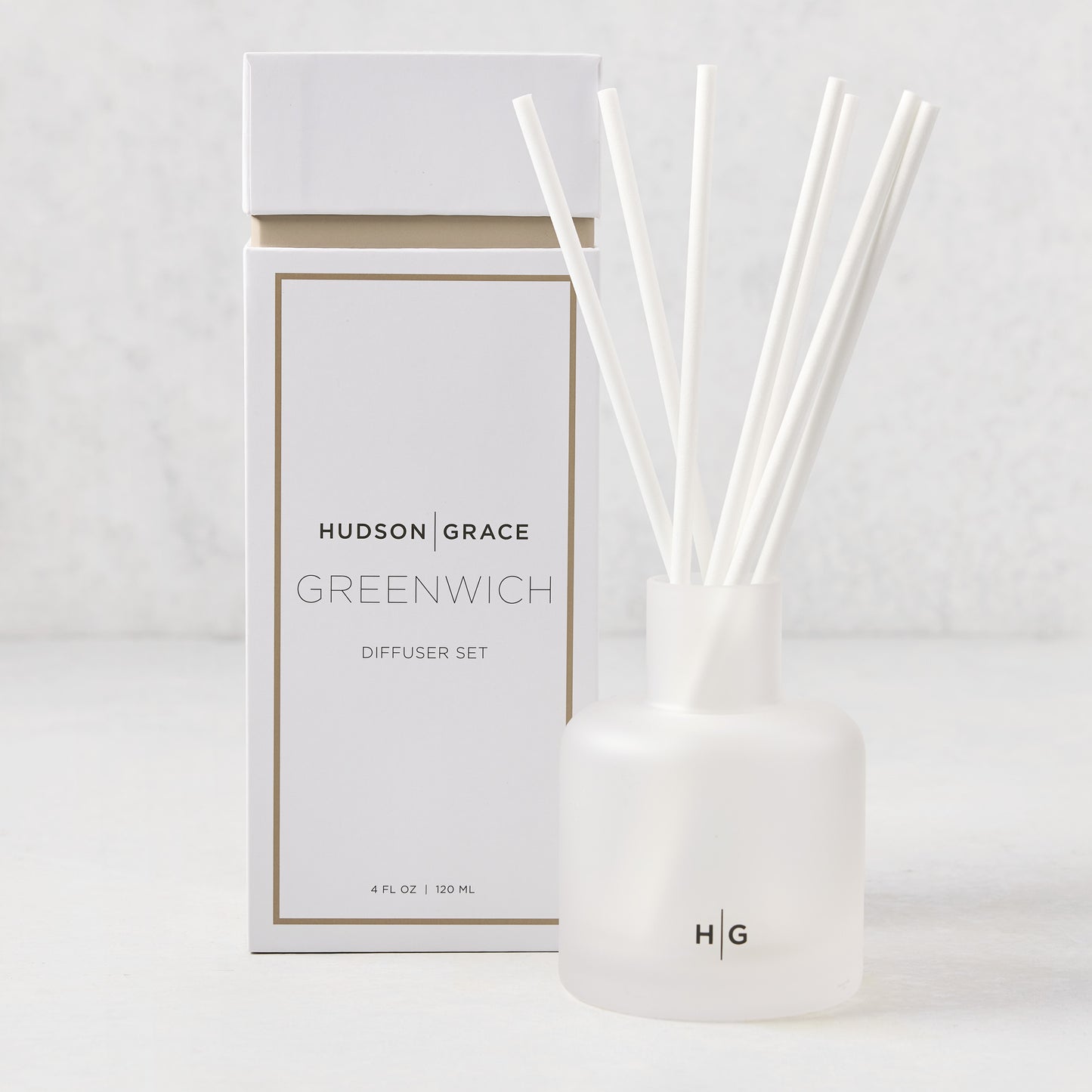 Hudson Grace Greenwich scented reed diffuser set: frosted white glass vessel with HG logo, 6 white fiber reeds, and white box.