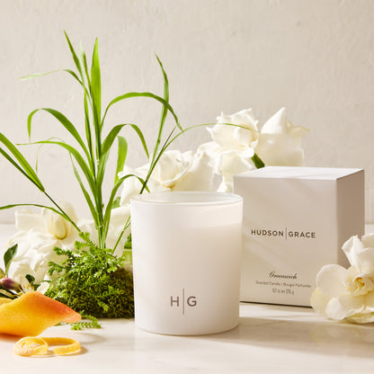 Hudson Grace Greenwich Scented Candle in a white glass vessel with HG logo, box, gardenias, and citrus peel.