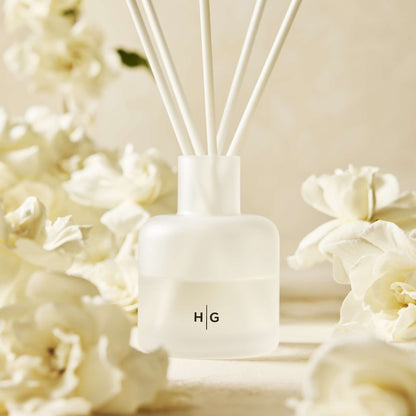 Hudson Grace Greenwich white frosted glass diffuser with reeds, surrounded by white gardenia flowers.