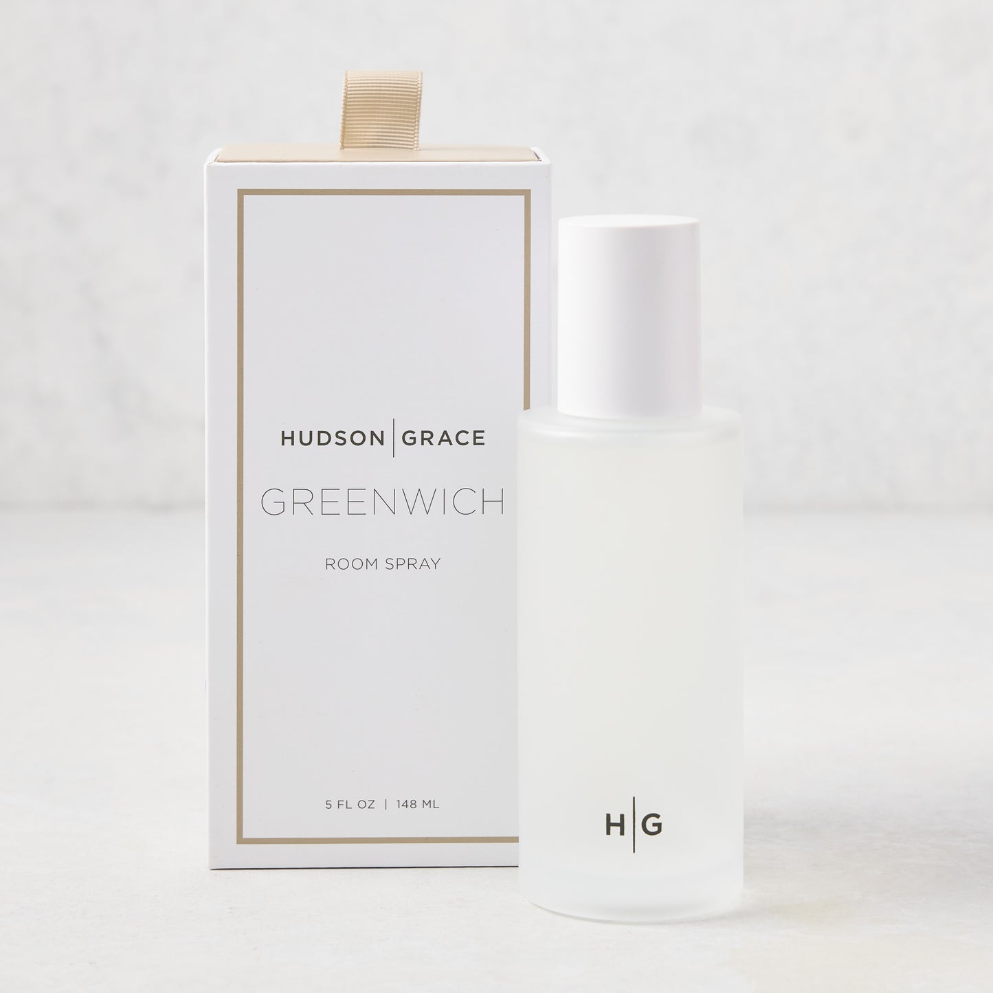 Hudson Grace Greenwich Room Spray: frosted glass bottle, white cap, next to white box with gold ribbon.
