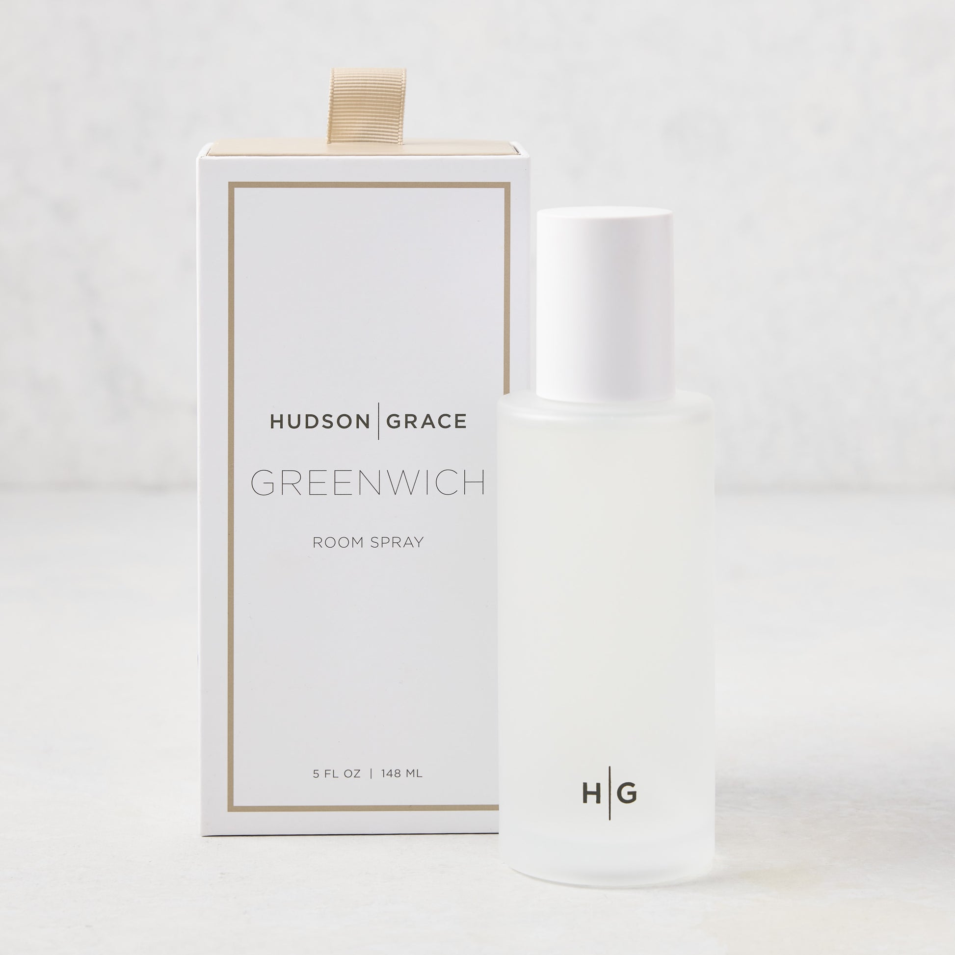 Hudson Grace Greenwich Room Spray: frosted glass bottle, white cap, next to white box with gold ribbon.
