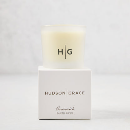 Hudson Grace Greenwich Scented Votive, a small candle in a frosted glass vessel with "HG" logo, on its white box.
