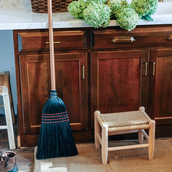 Hudson Grace handmade black broom with oak handle standing on a woven rug in a rustic kitchen setting