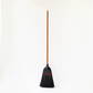 Hudson Grace handmade broom featuring a long oak wood handle and tightly bound black straw bristles with red stitching.