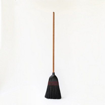Hudson Grace handmade broom featuring a long oak wood handle and tightly bound black straw bristles with red stitching.