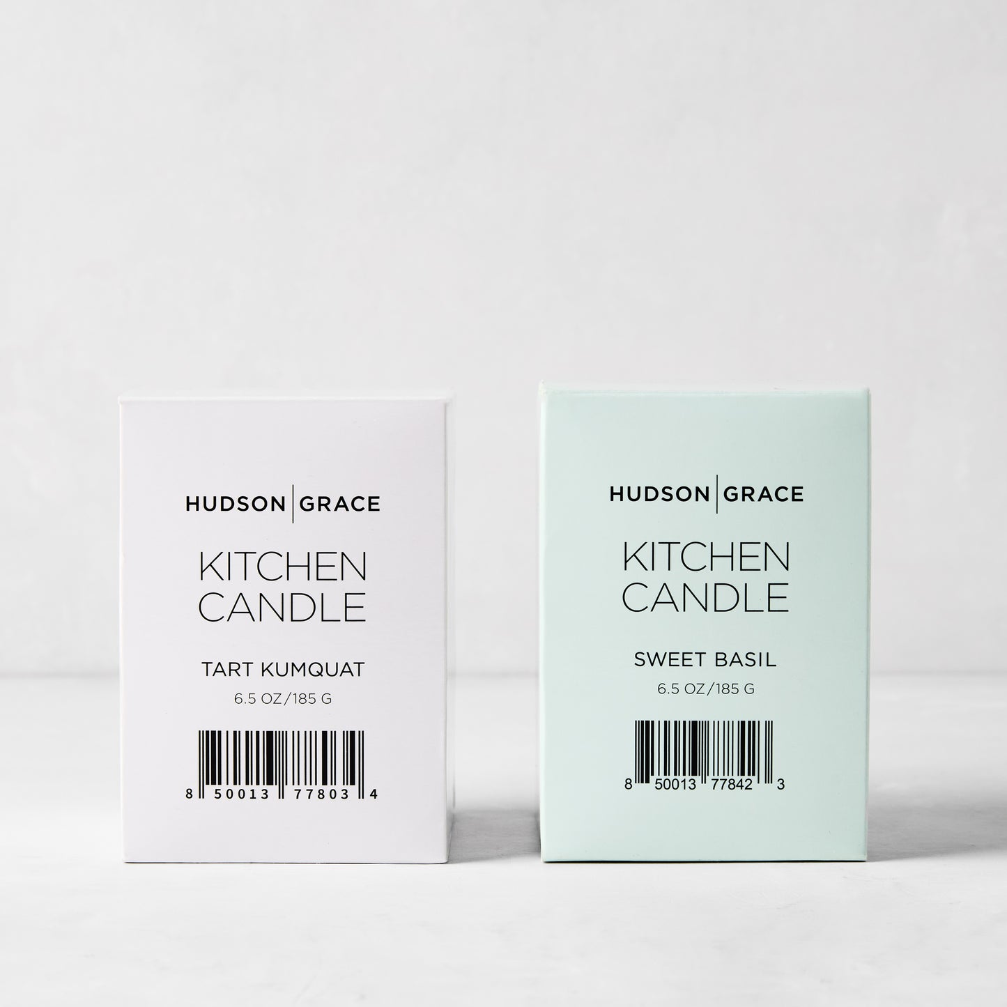Hudson Grace Kitchen Candle Bundle: white Tart Kumquat and light green Sweet Basil candles in elegant boxes.