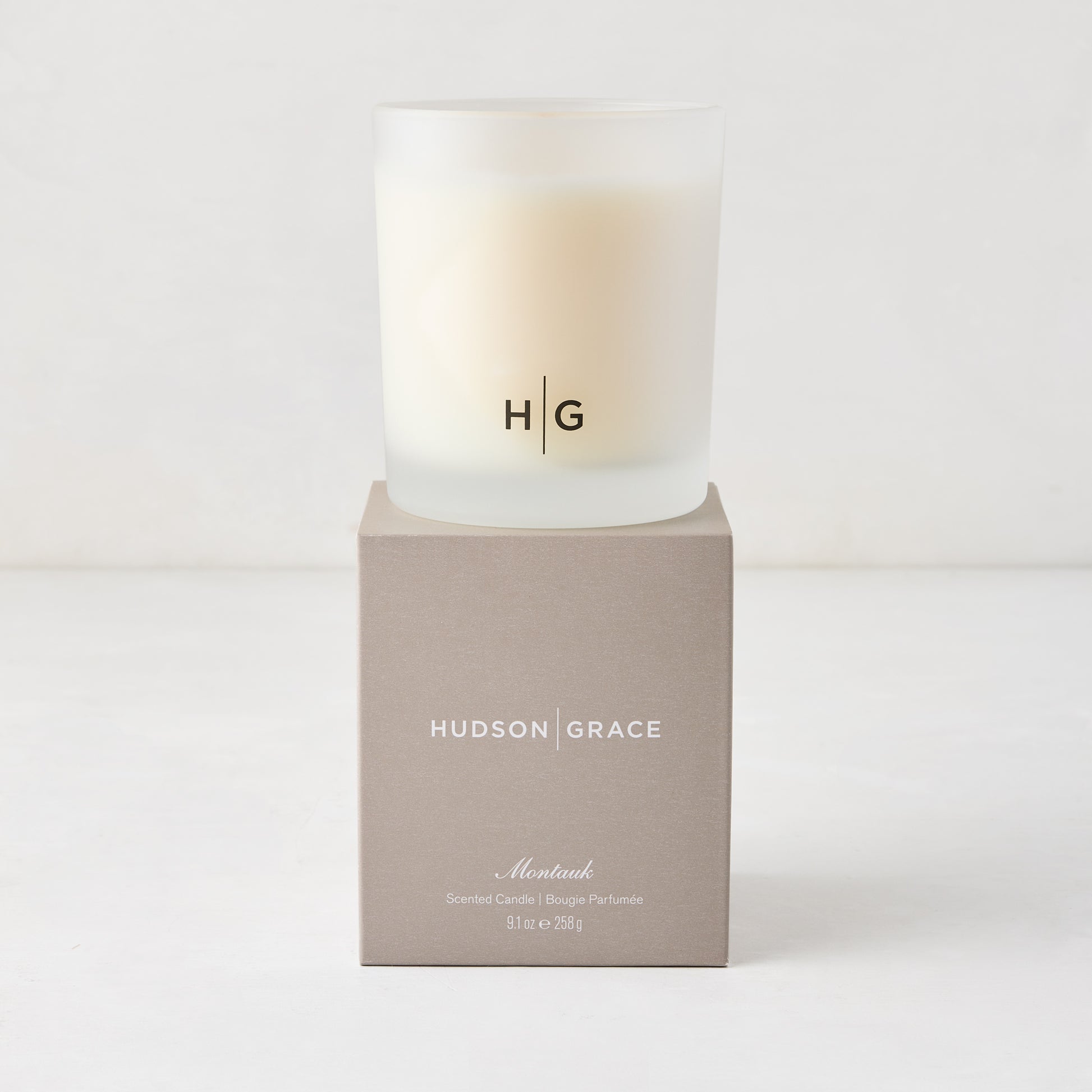 Hudson Grace Montauk Scented Candle in a frosted glass vessel with HG logo, on a matching beige box.