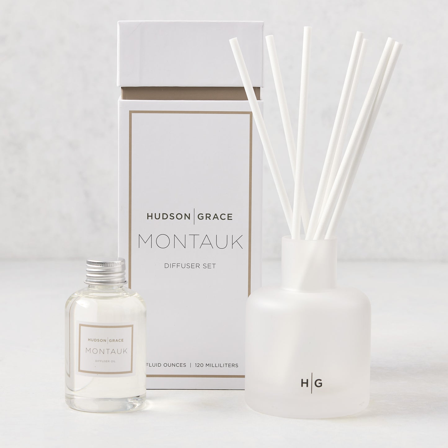 Hudson Grace Montauk Scented Reed Diffuser set: clear glass bottle, frosted glass vessel with white reeds, and white box.