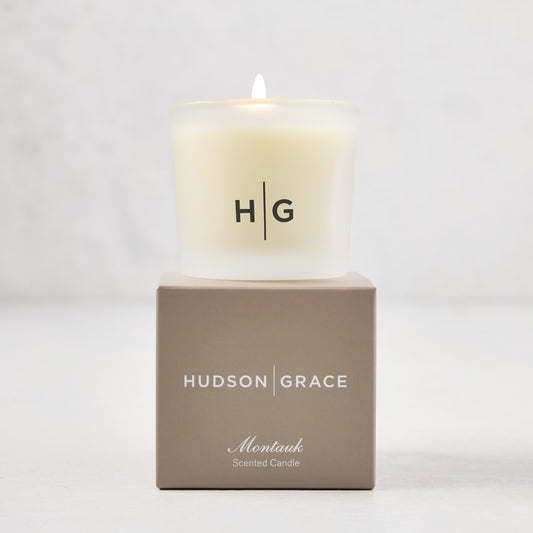 Hudson Grace Montauk Scented Votive candle in a frosted glass vessel with "HG" logo, on a taupe gift box.