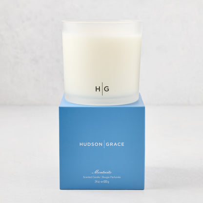 Hudson Grace Montecito 3-wick candle in a frosted glass vessel with HG logo, on a blue gift box.