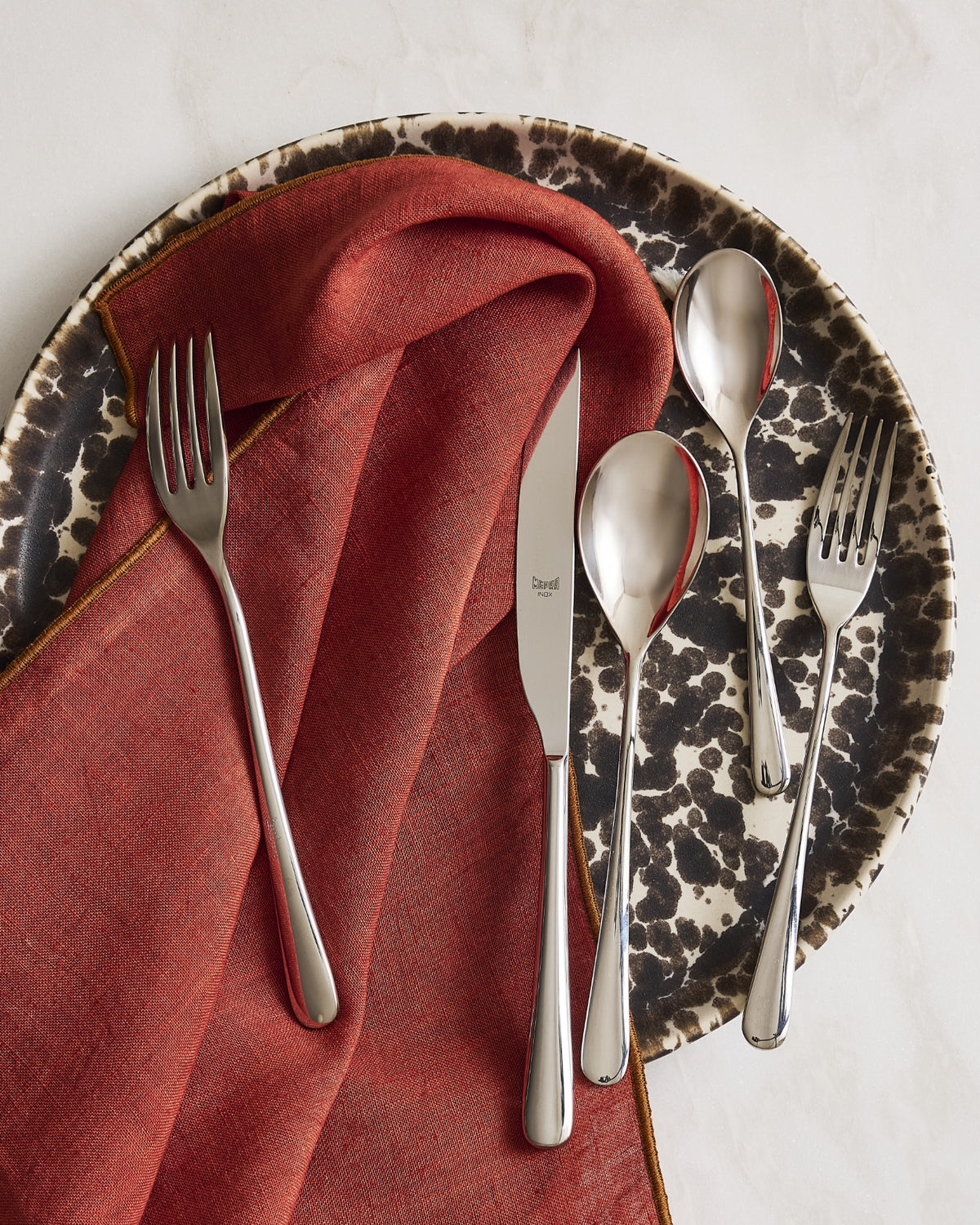 Hudson Grace Neve stainless steel flatware with a Nuno splatter plate and rust linen napkin