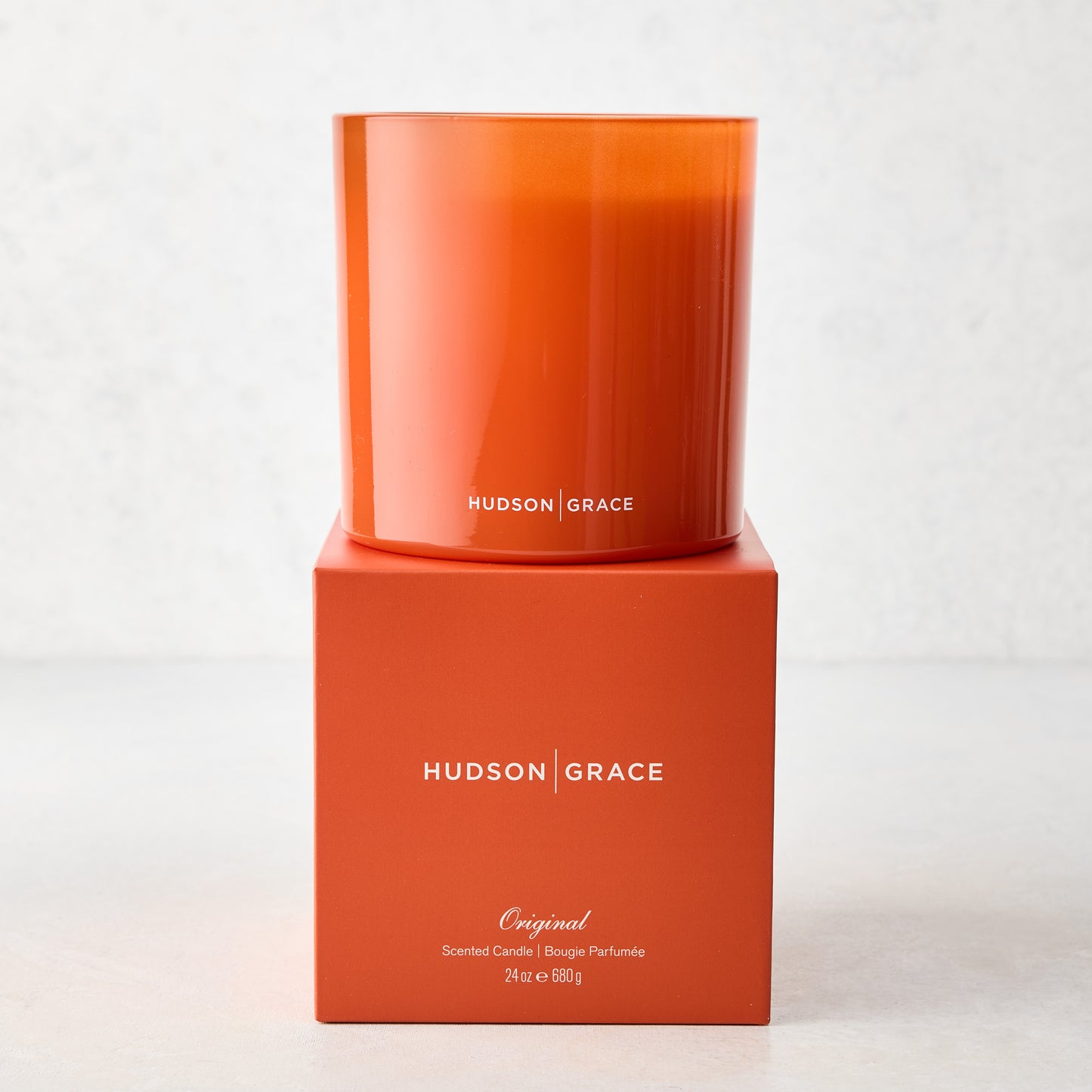 Hudson Grace Original 3-Wick Scented Candle in an orange glass vessel on its matching orange box.