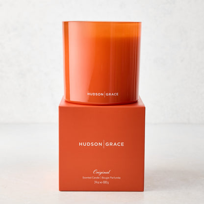 Hudson Grace Original 3-Wick Scented Candle in an orange glass vessel on its matching orange box.